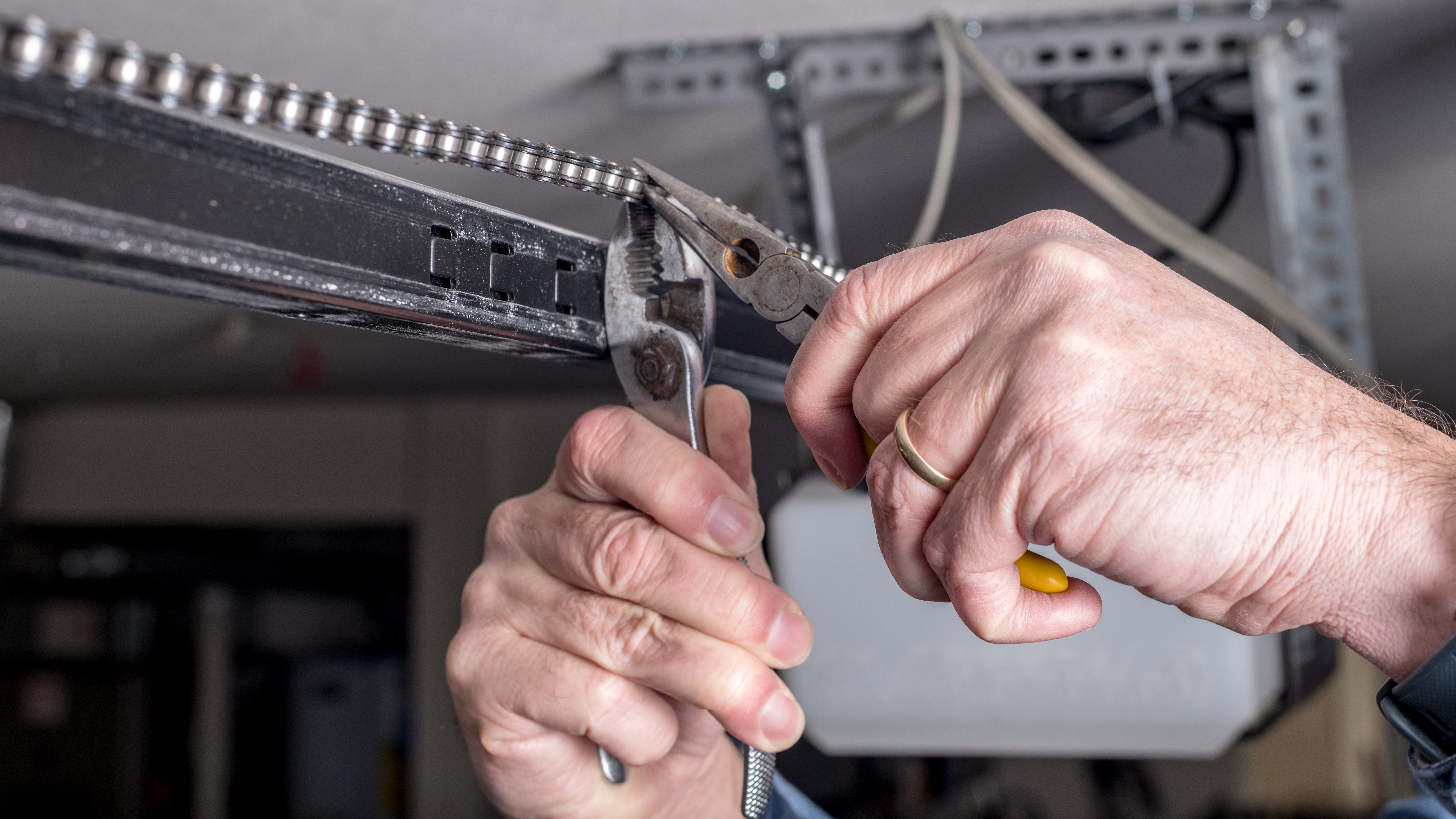 Man uses pliers for diy garage door repair on an opener chain.